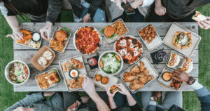 Picture of friends gathered around a table enjoying a spread of food in relation to foodservice in 2024.